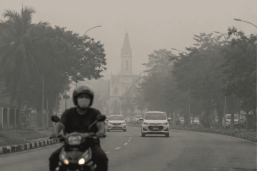 Motorcyclist wearing a face mask riding through hazy street conditions in Sarawak
