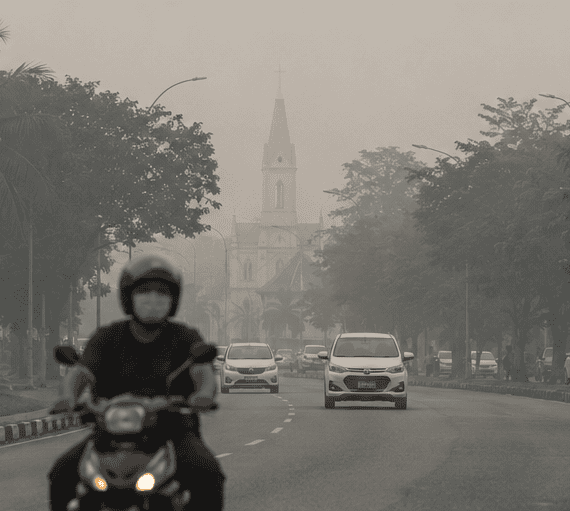 Motorcyclist wearing a face mask riding through hazy street conditions in Sarawak