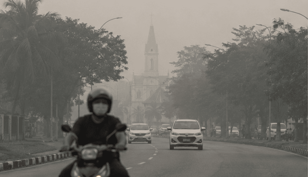 Motorcyclist wearing a face mask riding through hazy street conditions in Sarawak